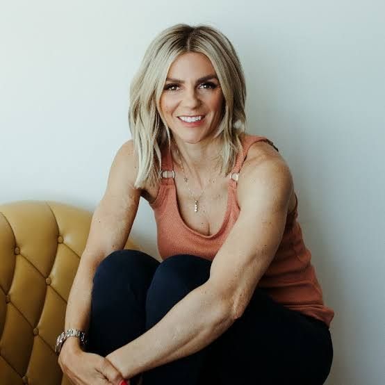 Smiling blonde woman in a coral top sitting on a mustard sofa