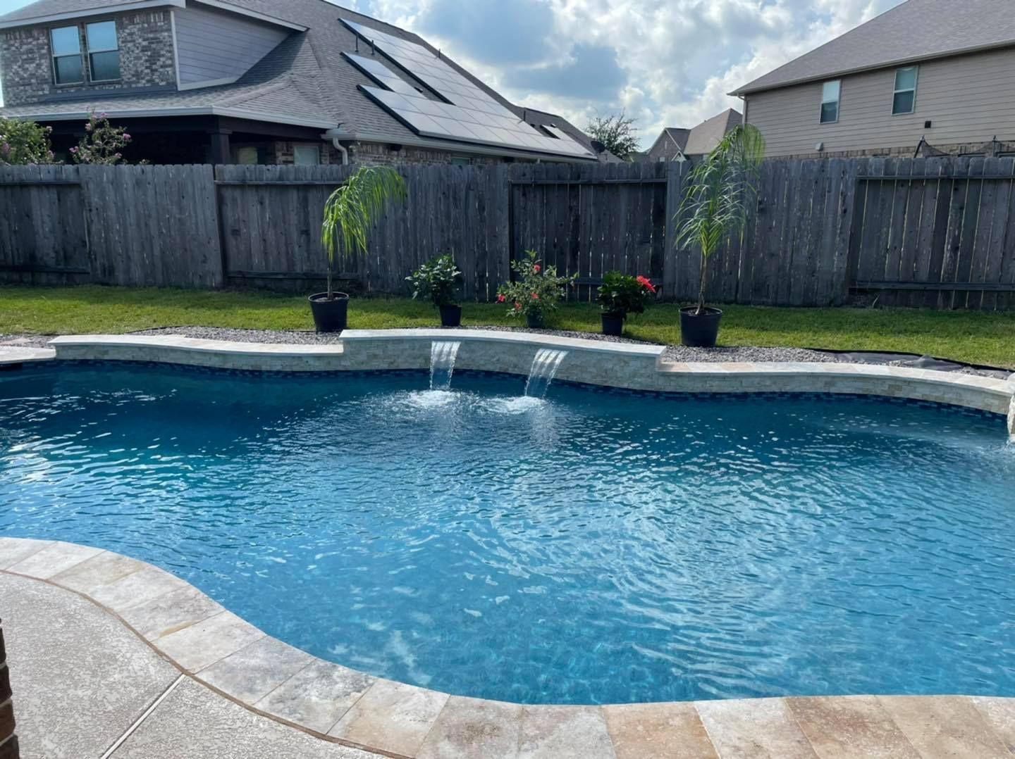 A large swimming pool with a waterfall in the backyard of a house.