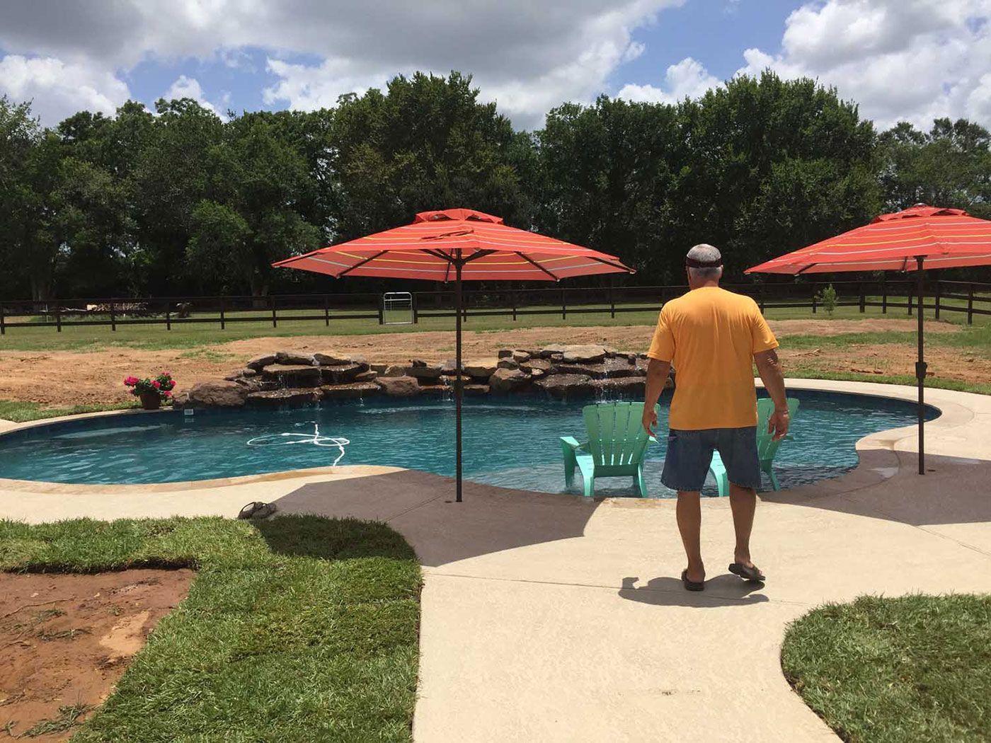 A man in a yellow shirt is standing in front of a swimming pool.