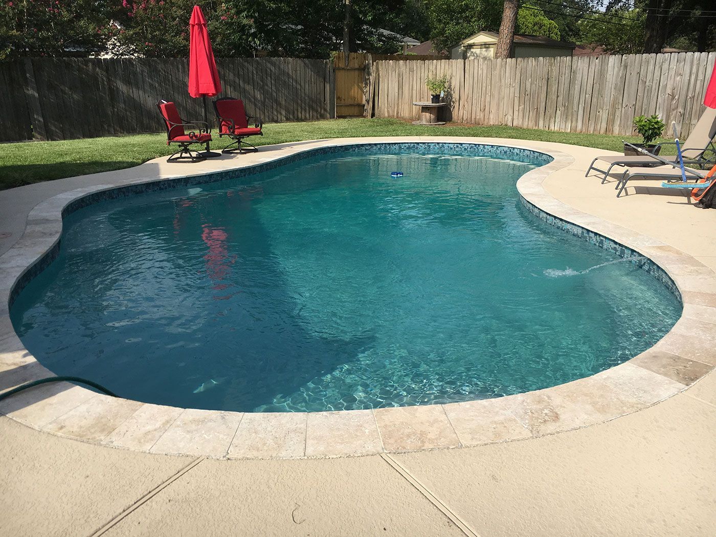 A large swimming pool surrounded by chairs and umbrellas in a backyard.