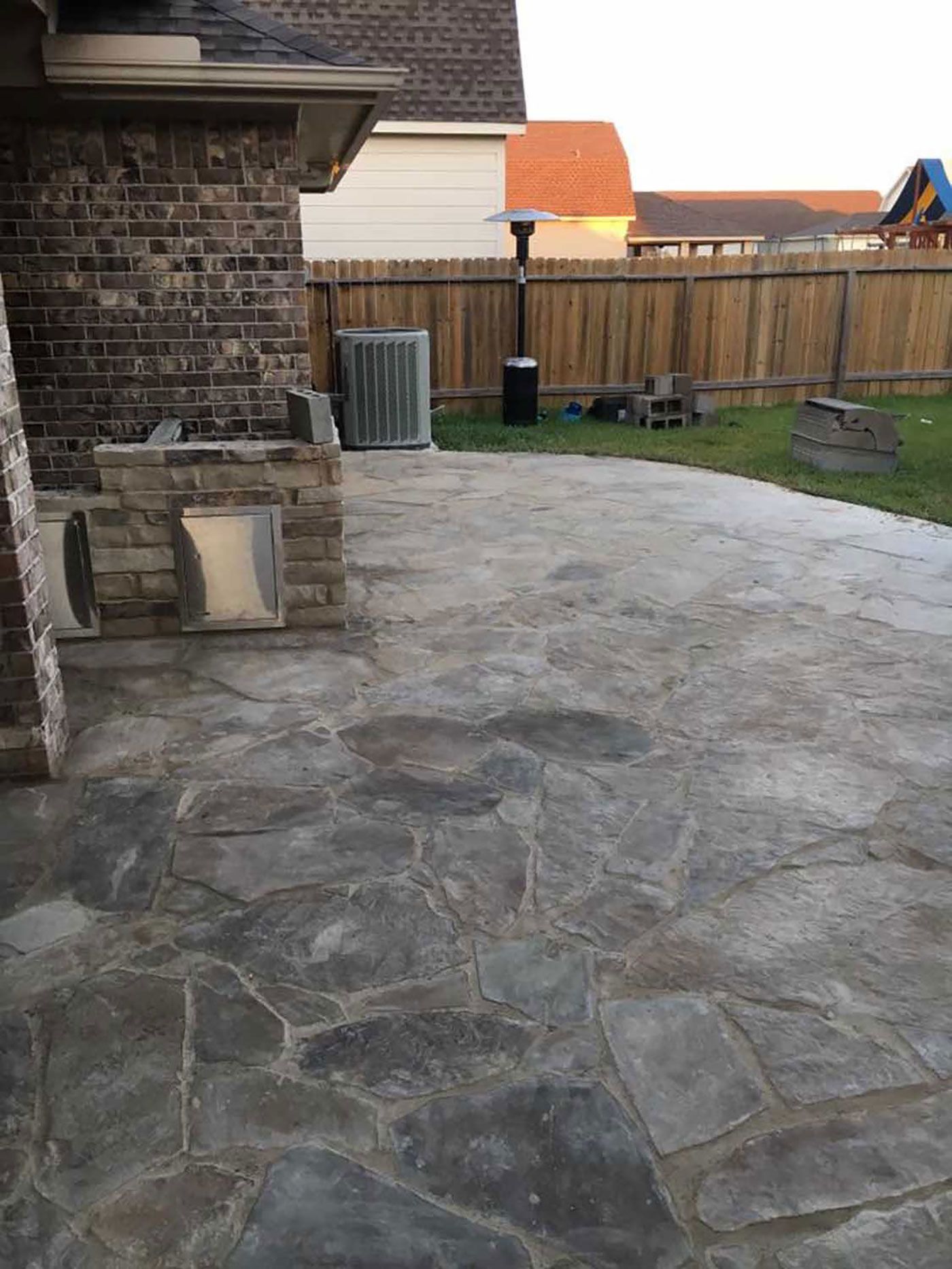 A patio with a brick wall and a wooden fence in the backyard of a house.