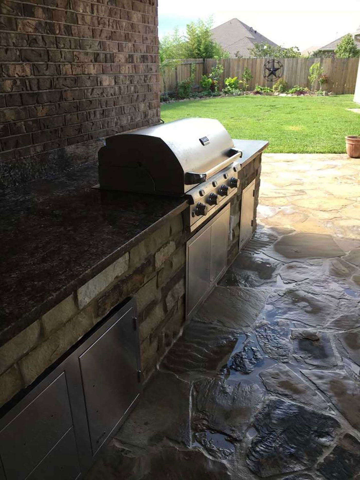 A grill is sitting on top of a stone counter next to a brick wall.