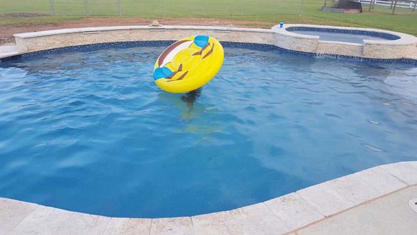A yellow smiley face float is floating in a swimming pool.