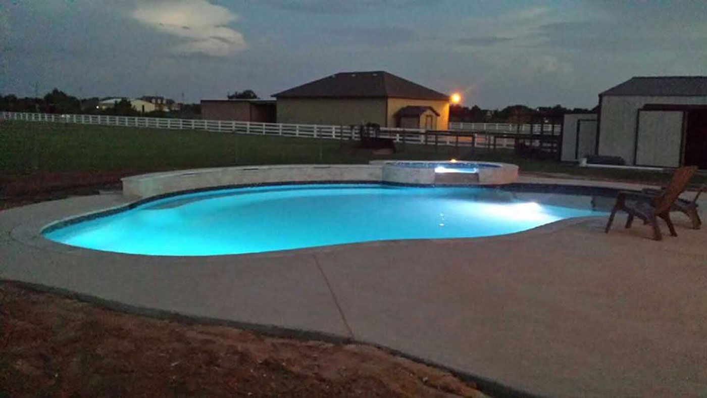 A large swimming pool is lit up at night in a backyard.