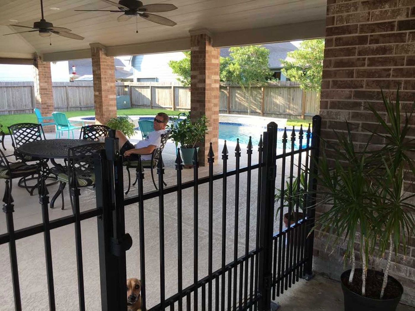 A man is sitting on a patio next to a pool behind a fence.