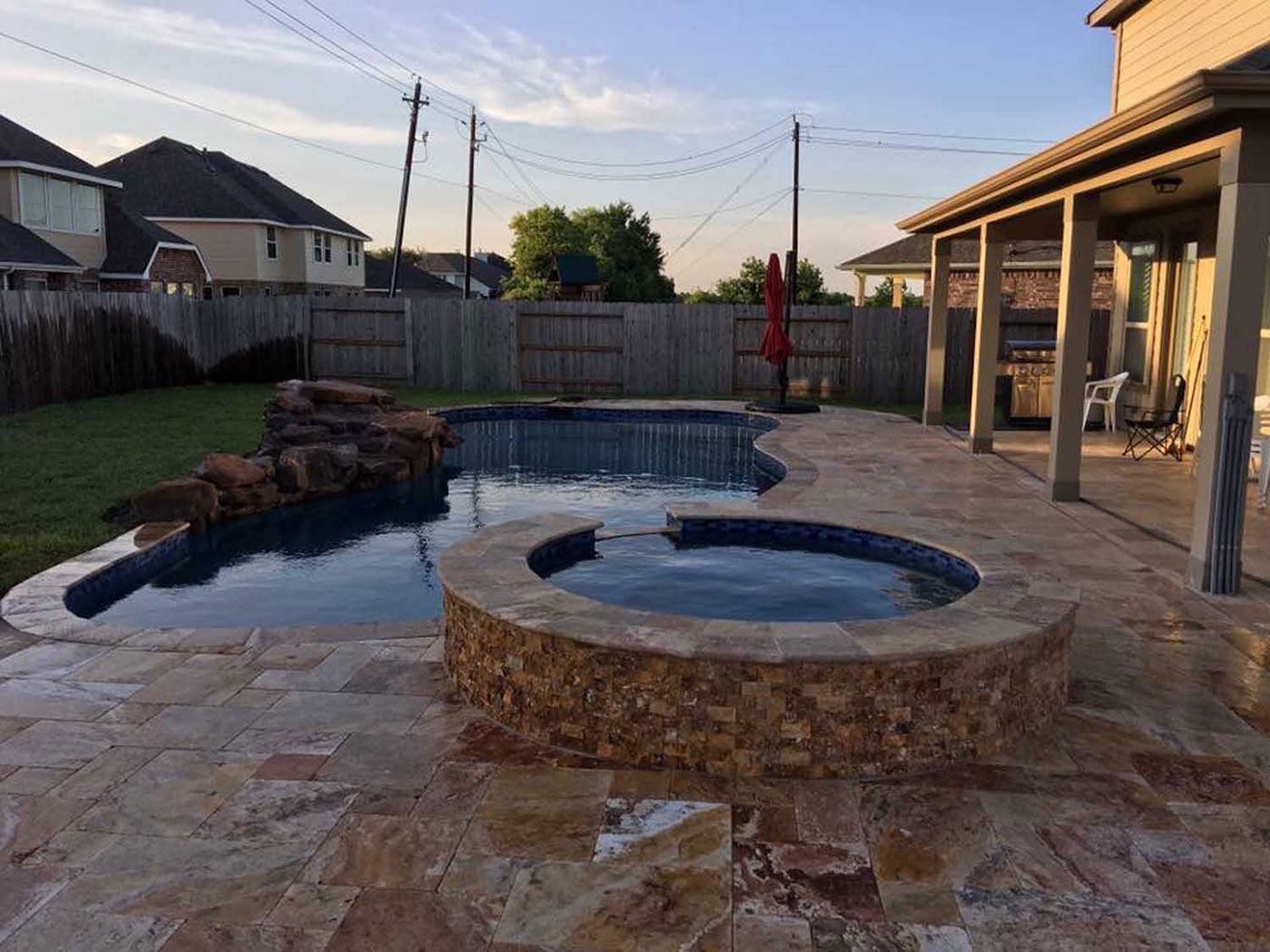 A large swimming pool with a hot tub in the backyard of a house.