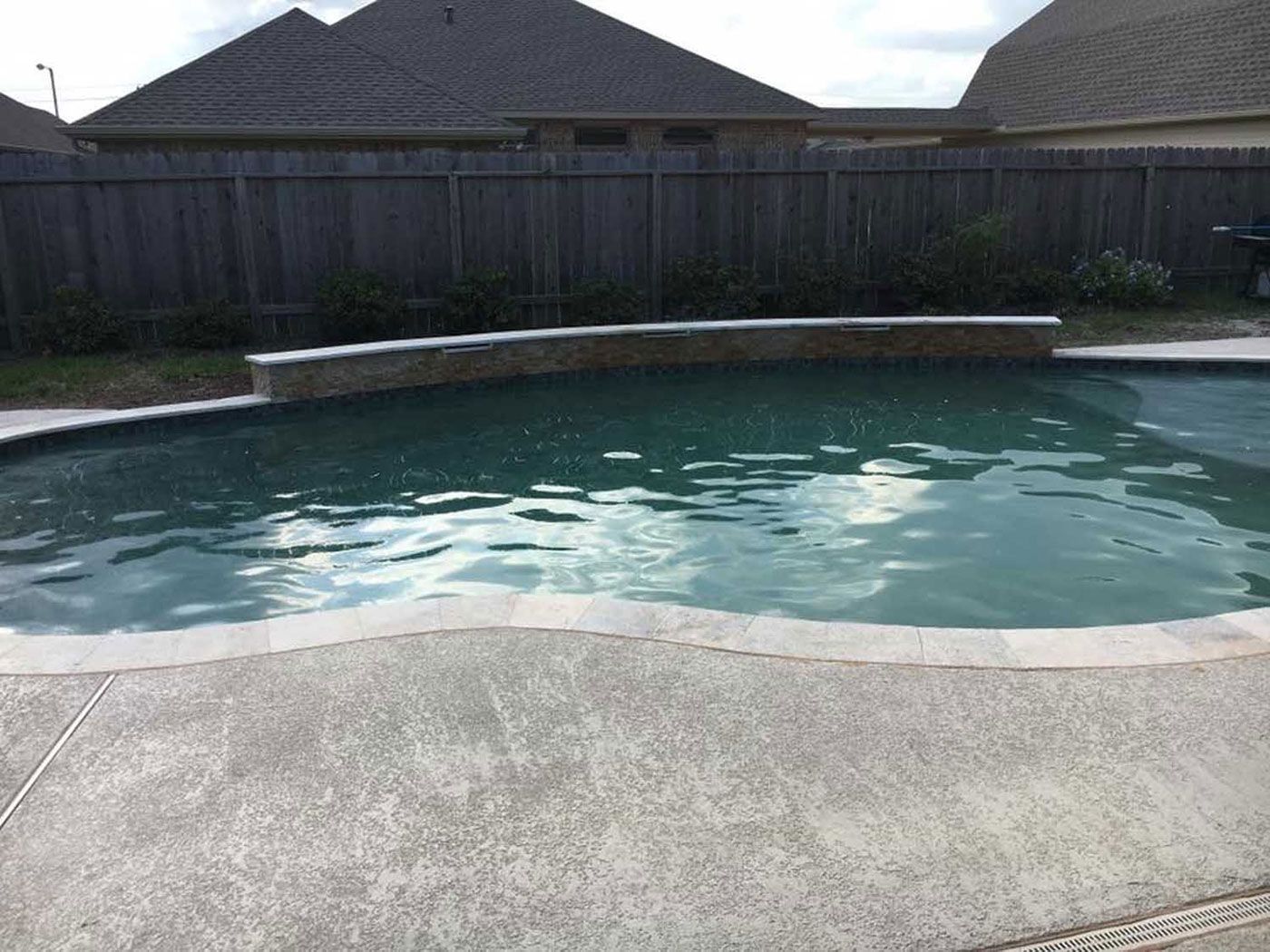 A large swimming pool in the backyard of a house with a fence in the background.