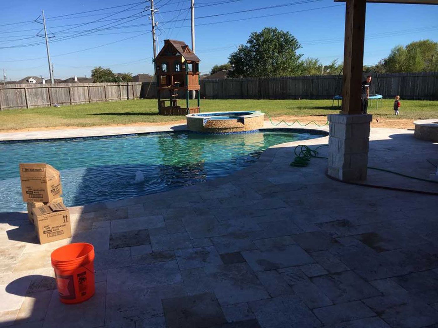 A bucket of orange paint is sitting next to a swimming pool.