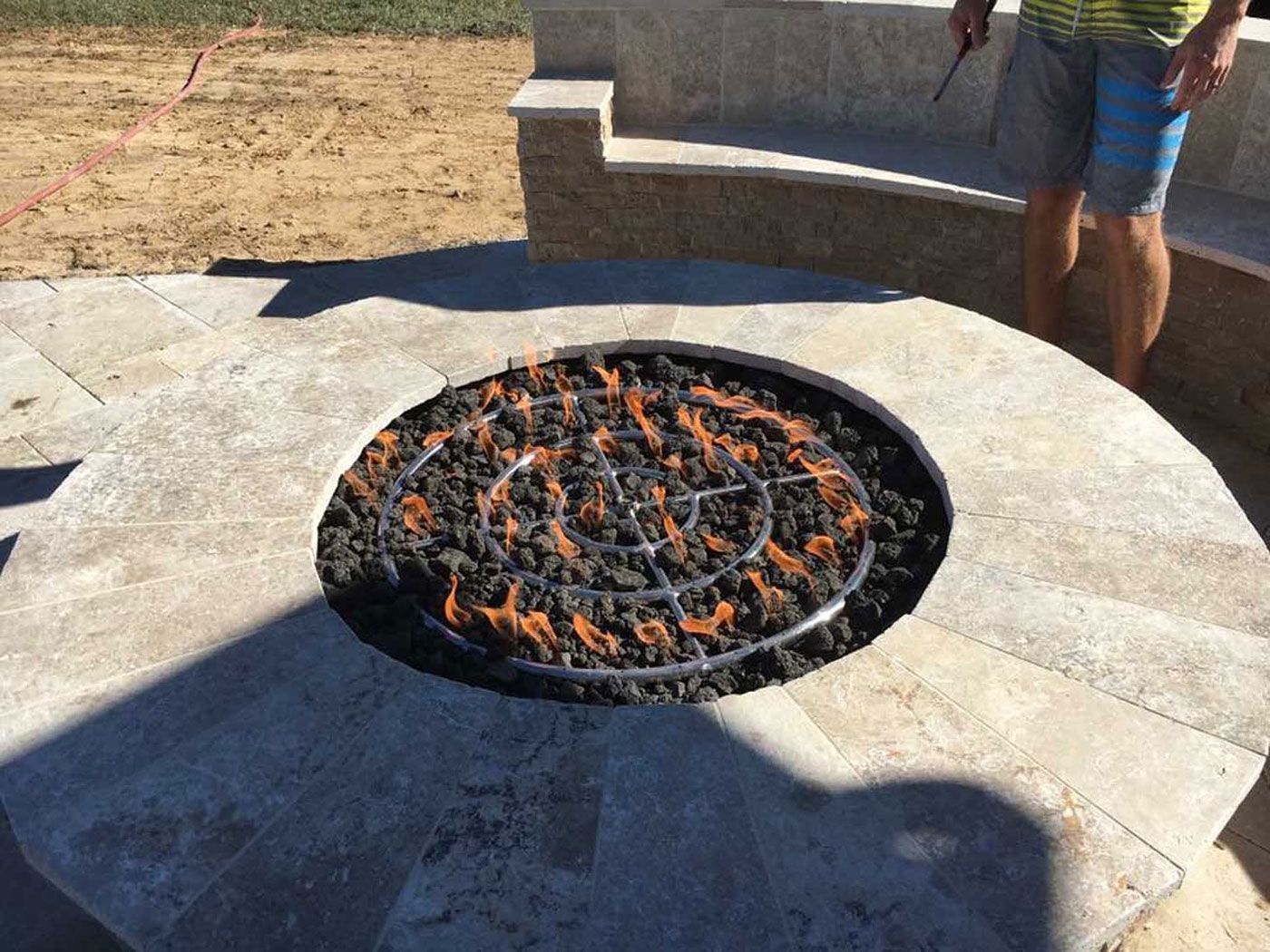 A man is standing next to a fire pit on a patio.