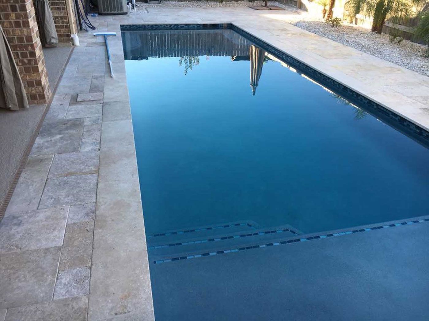 A large swimming pool with a brick border and a reflection of a building in the water.