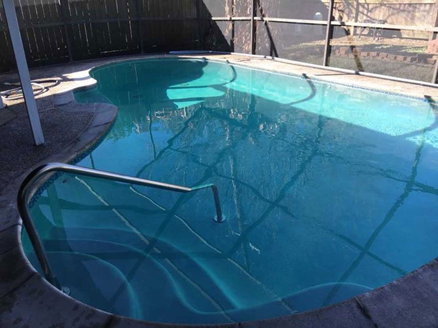 A large swimming pool surrounded by a screened in area and a fence.