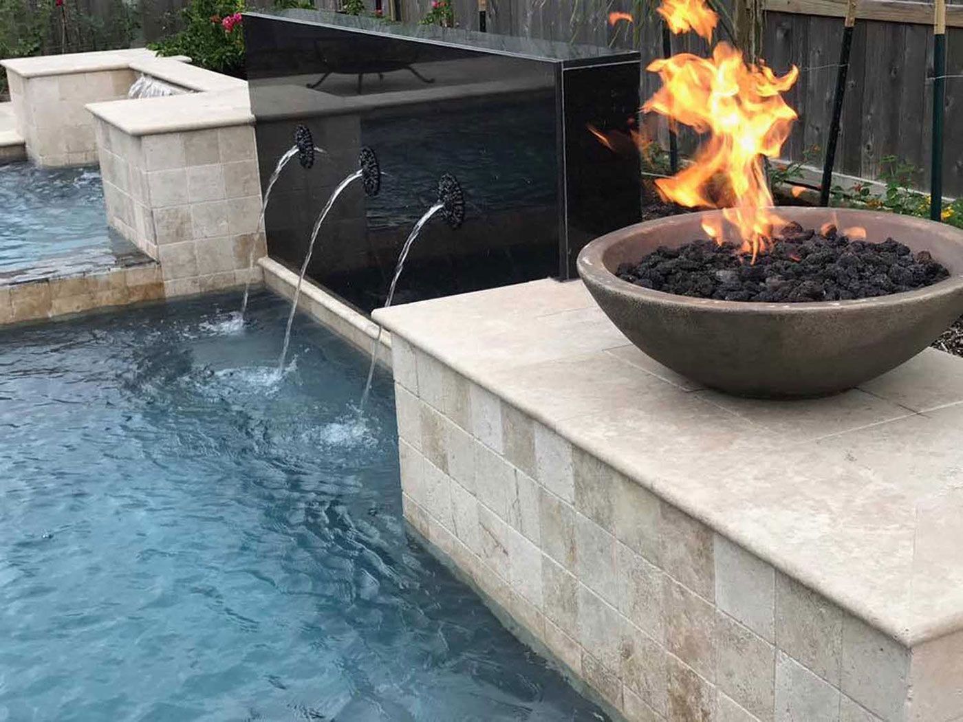 A fire pit is sitting next to a pool with water coming out of it.