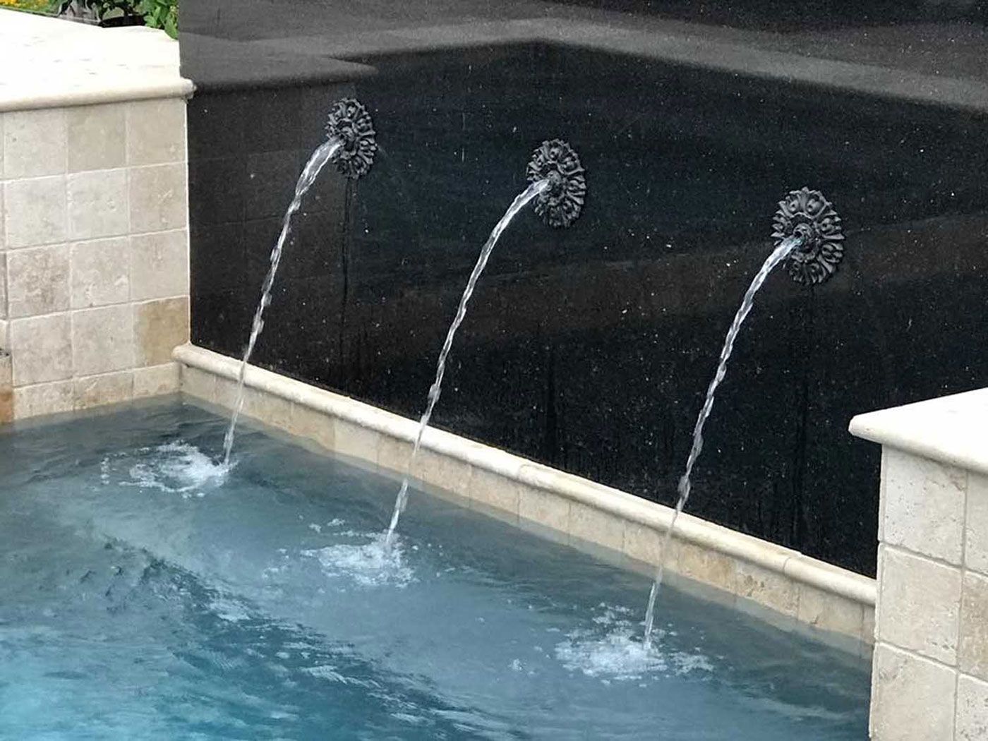 Three water fountains are spraying water into a pool.