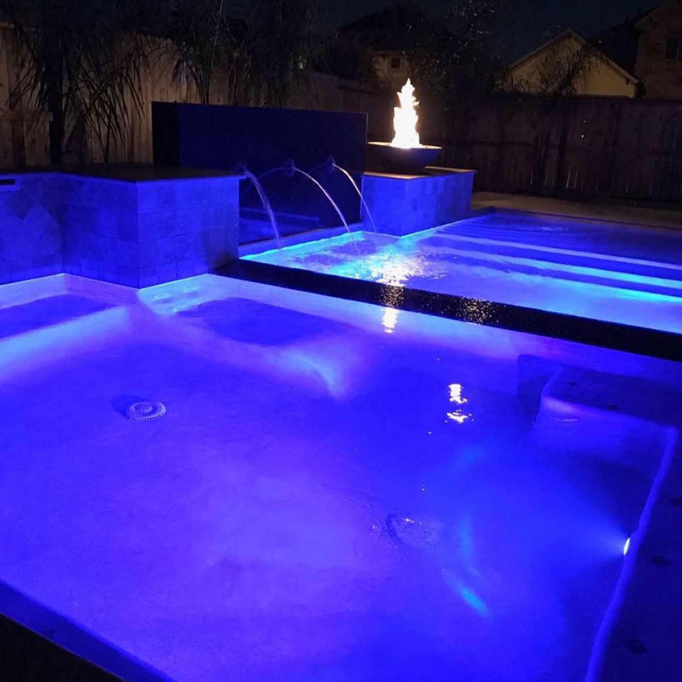 A swimming pool is lit up with blue lights at night