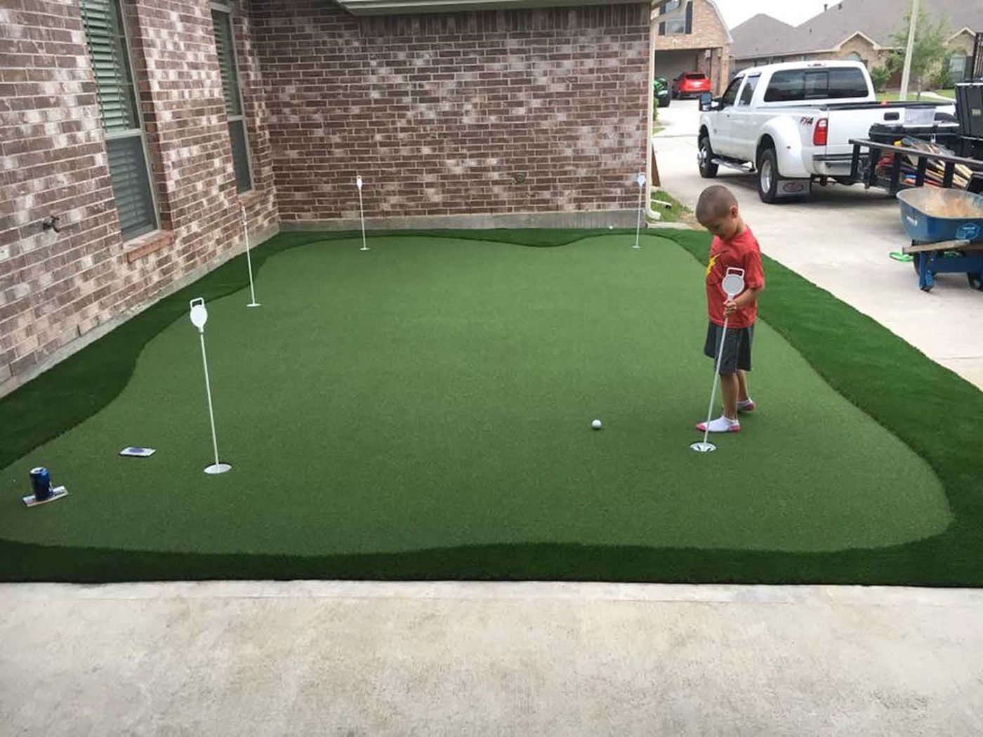 A young boy is putting a golf ball on a putting green.