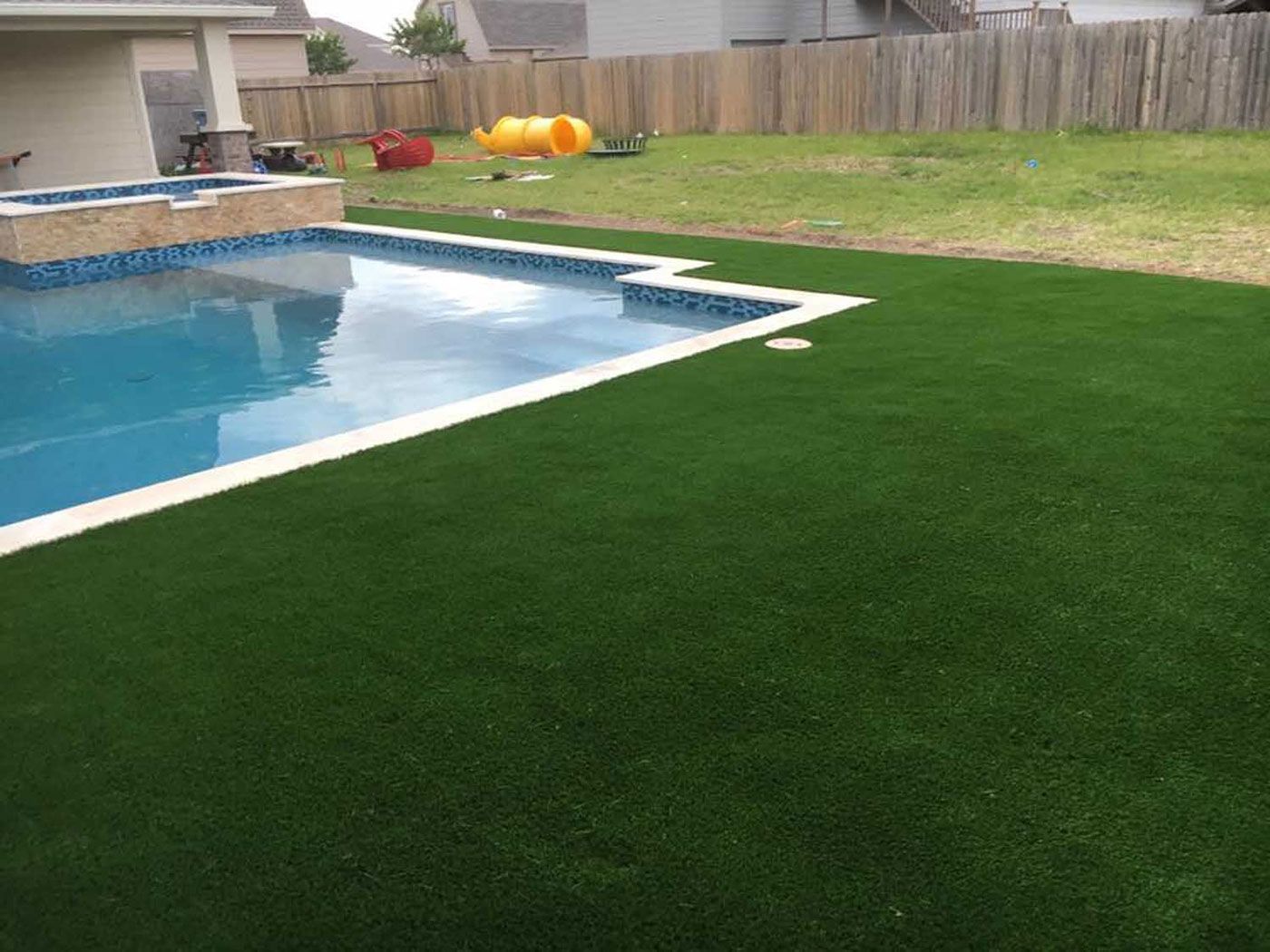 A swimming pool surrounded by a lush green lawn in a backyard.