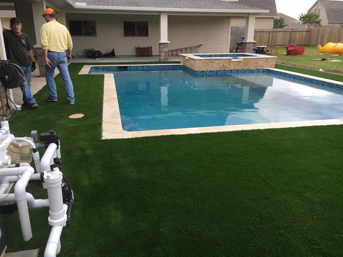 Two men are standing next to a swimming pool in a backyard.