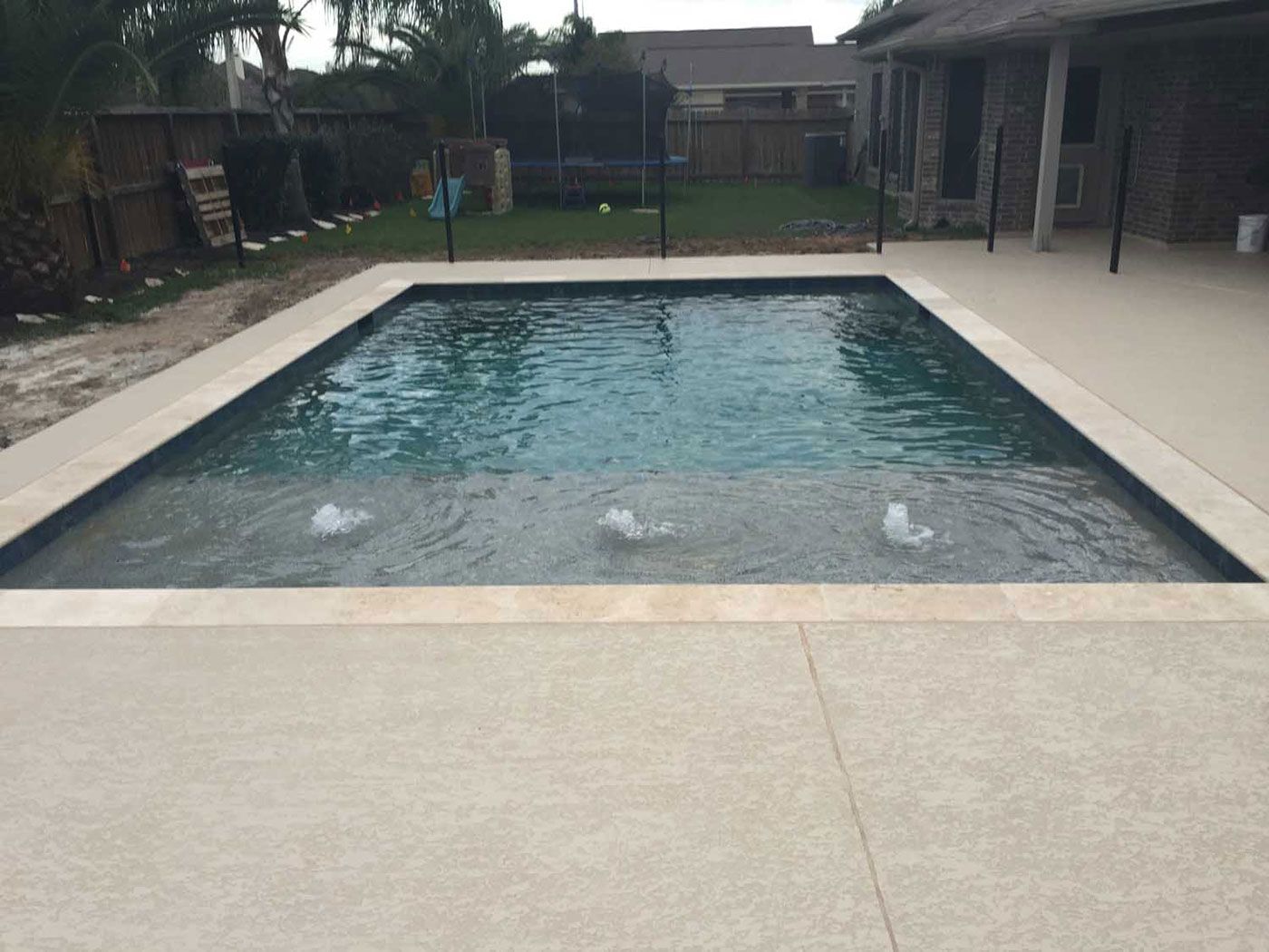 A large rectangular swimming pool is surrounded by a concrete patio.