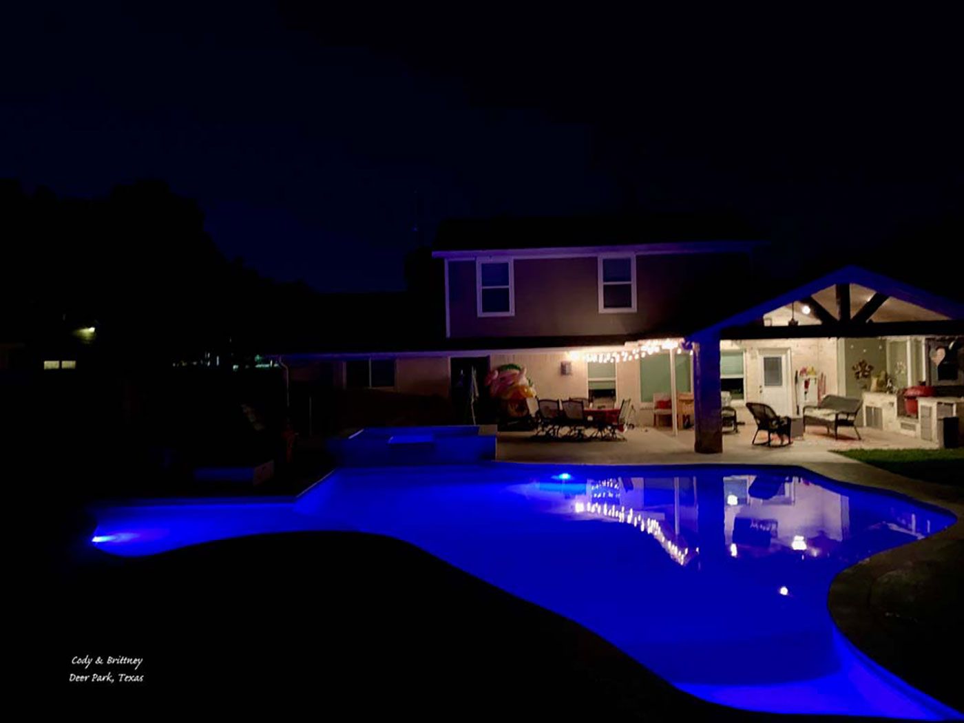 A large swimming pool is lit up at night in front of a house