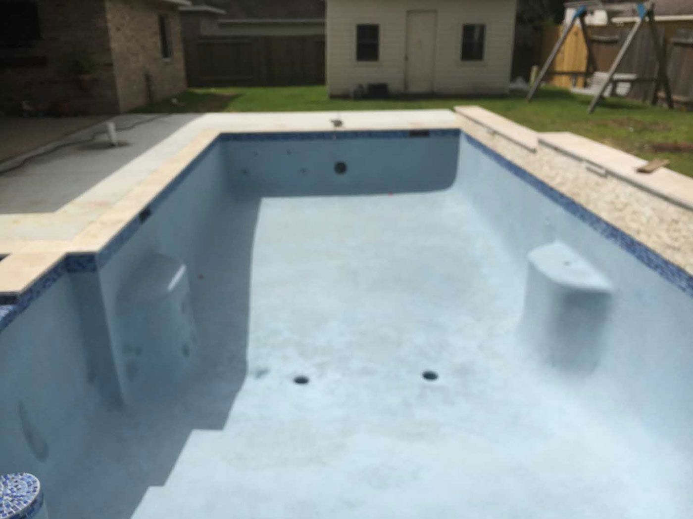 An empty swimming pool with a house in the background