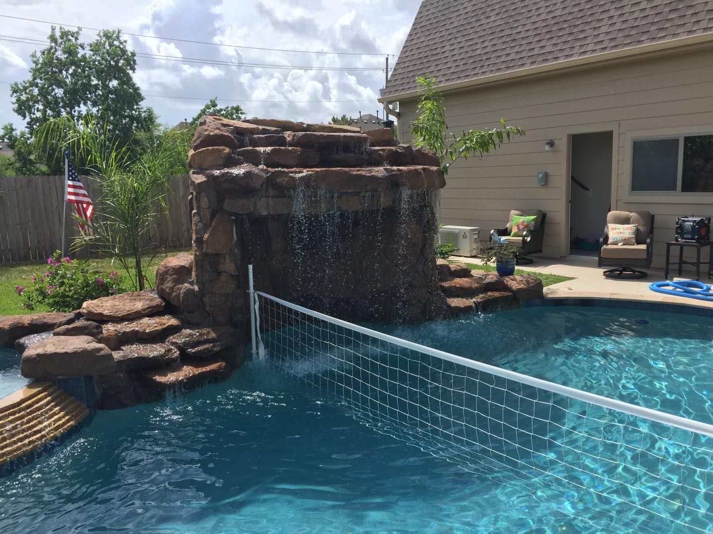 A swimming pool with a waterfall and a volleyball net in front of a house.