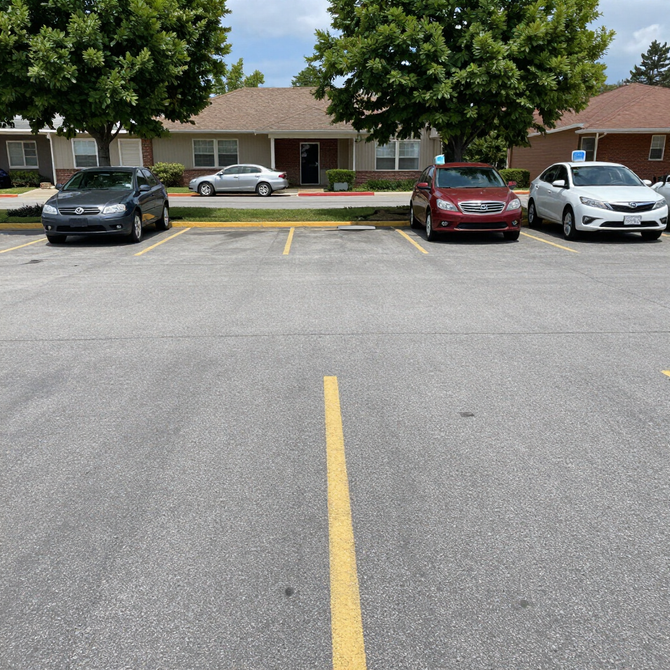 Parking lot with three cars parked in front of a brick apartment building and trees.