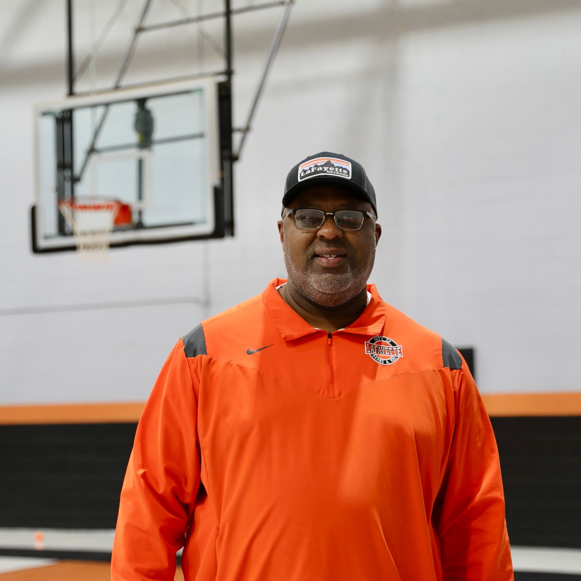 Football coach with arms crossed, standing on a football field. He wears a navy polo shirt and gray pants.