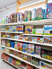 Woman smiling, holding several plush toys in a brightly lit toy store, surrounded by shelves of merchandise.