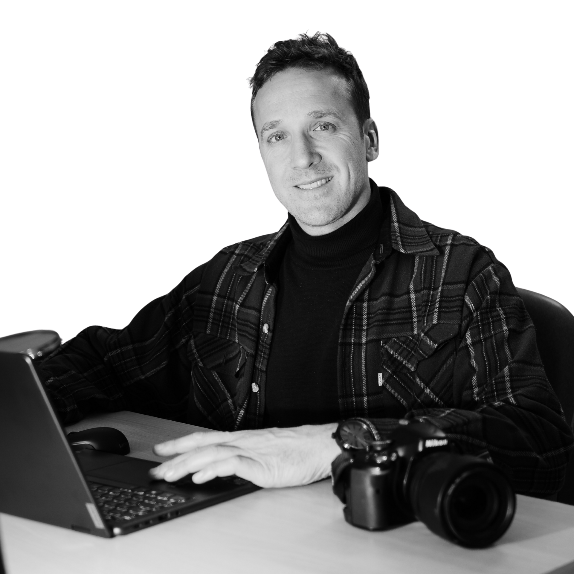 Un homme est assis à un bureau avec un ordinateur portable et un appareil photo