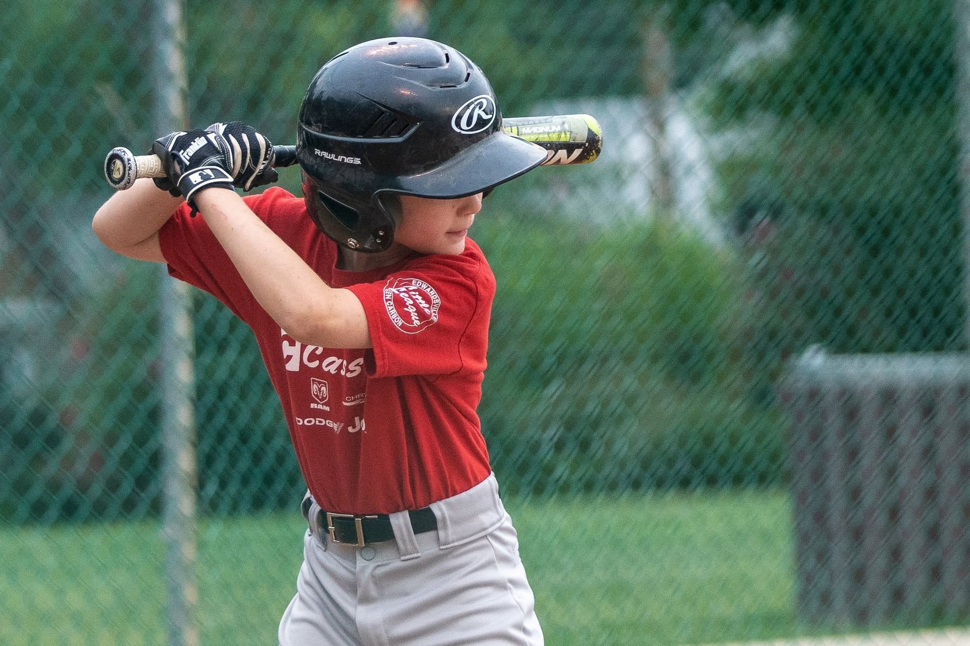 Young baseball player in red shirt and black helmet swinging a bat on a field