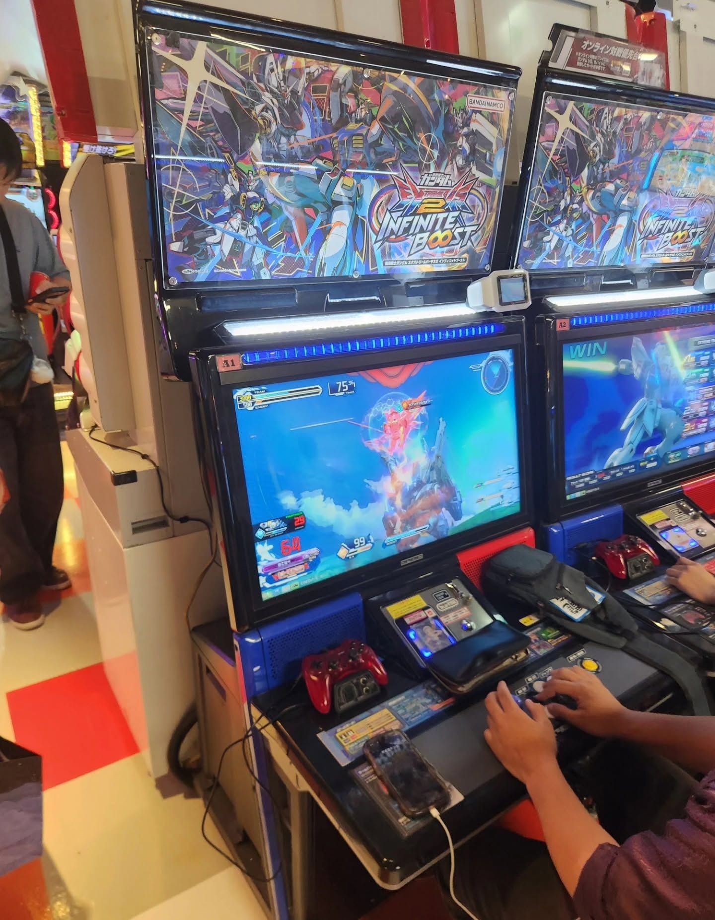 Person playing a colorful arcade fighting game on two stacked game cabinets in an arcade.
