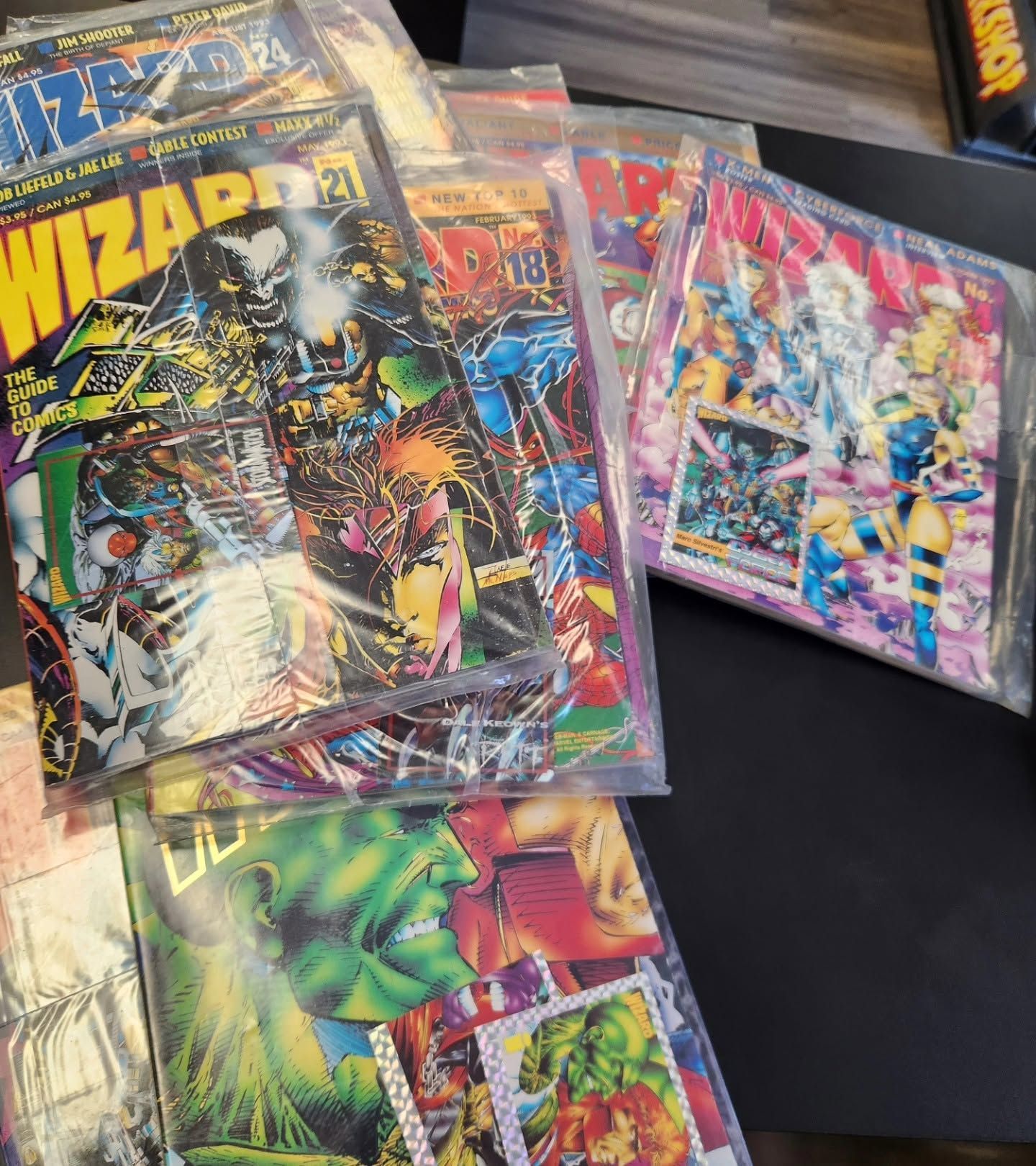 Stack of colorful Wizard trading card packs in plastic sleeves on a black surface