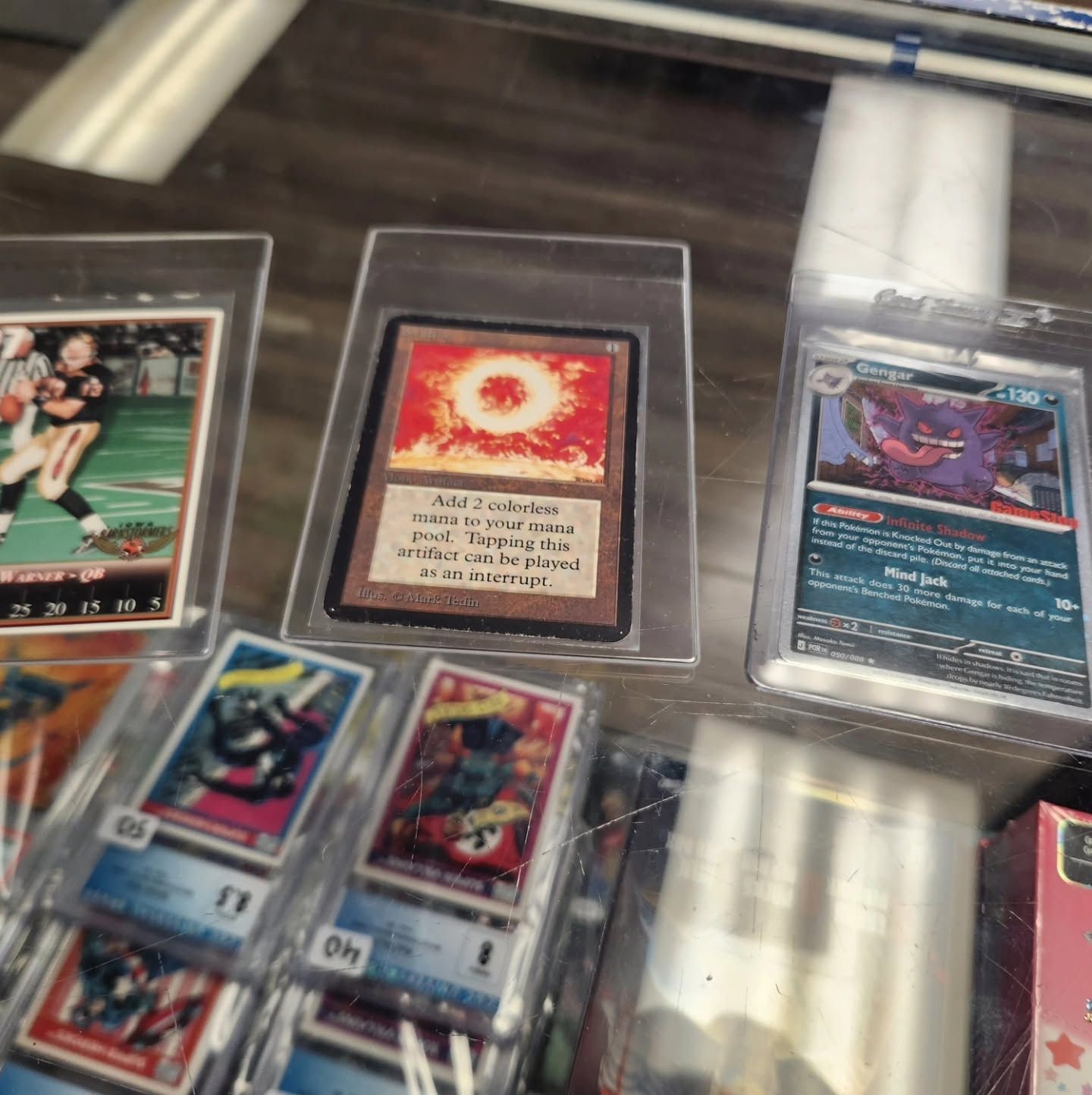Trading cards in sleeves on a wooden table, including a holographic card and a red-bordered card.