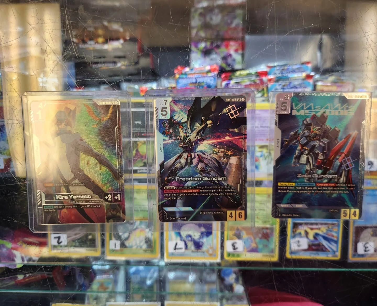 Three colorful trading cards displayed in a glass case, with more cards and reflections in the background.