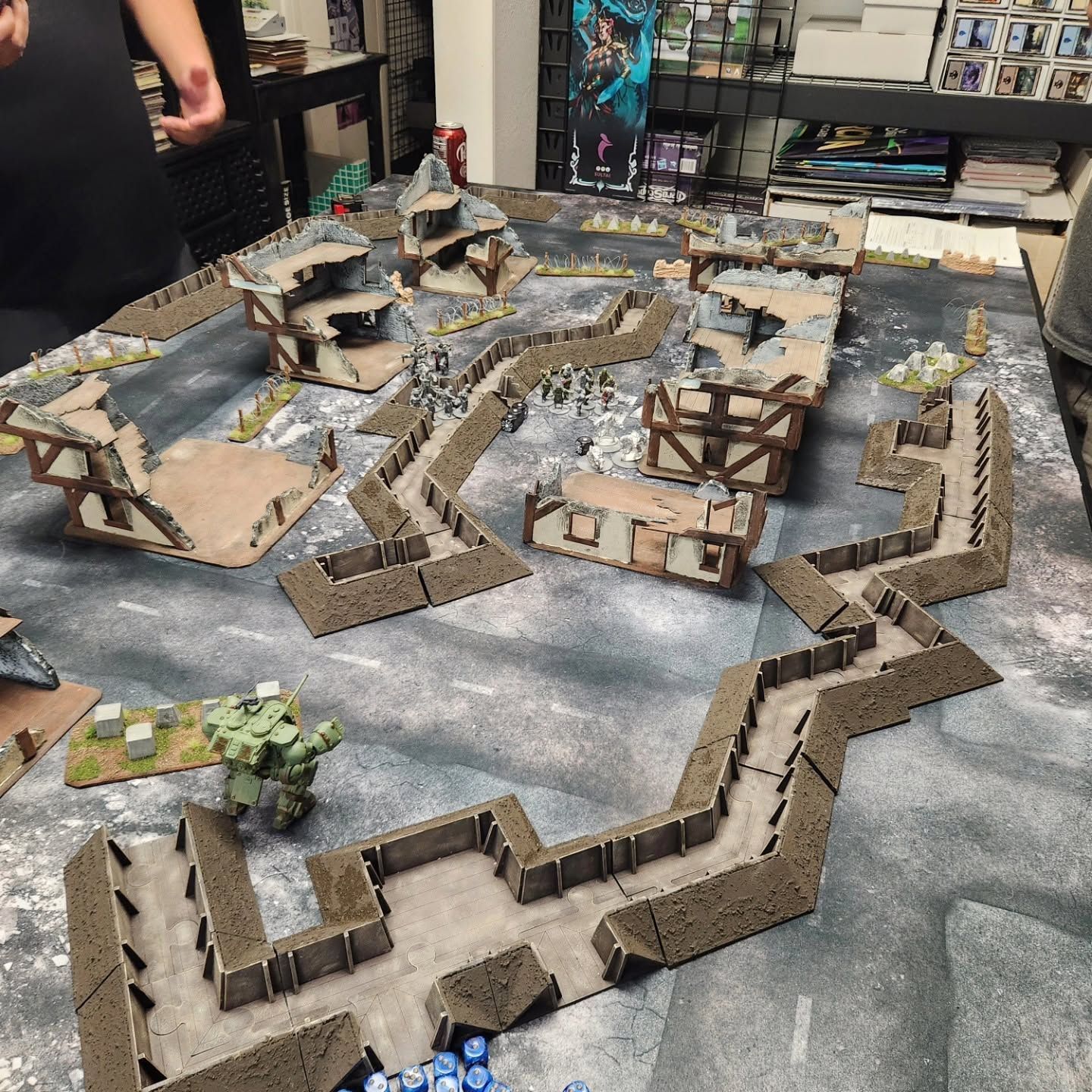 Tabletop miniature terrain with cardboard walls, pathways, and buildings on a game table