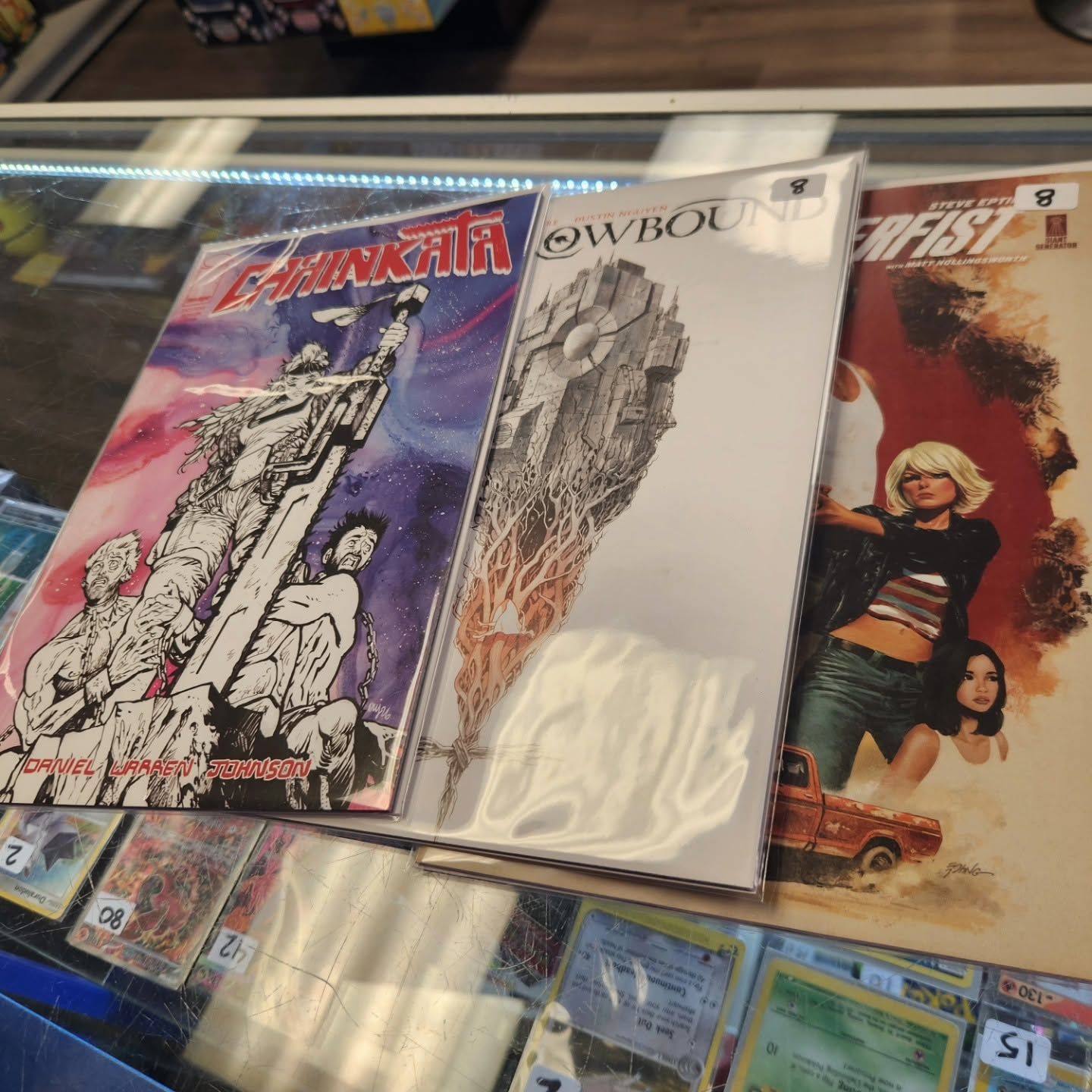 Three comic books in plastic sleeves on a store rack, including one titled “Cowboy” and a red cover on the left.