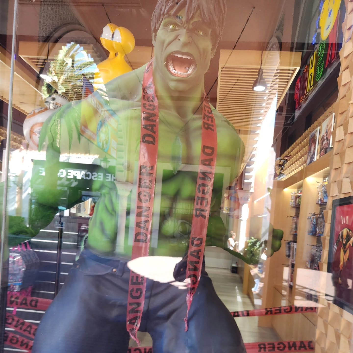 Green Hulk statue in a storefront window, mouth open and wearing a red lanyard.