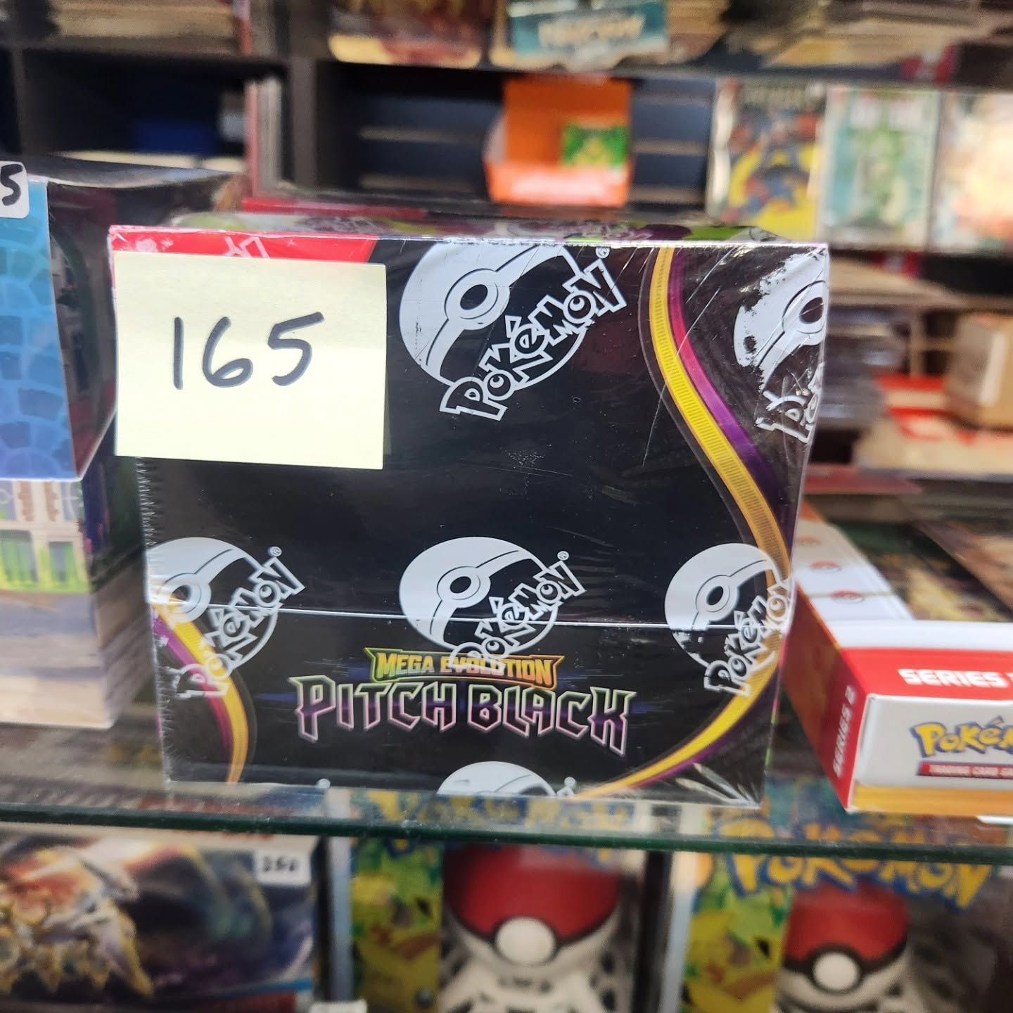 Pokémon TCG Sword & Shield: Fusion Strike booster box, black with skull art, on a store shelf with price tag 165