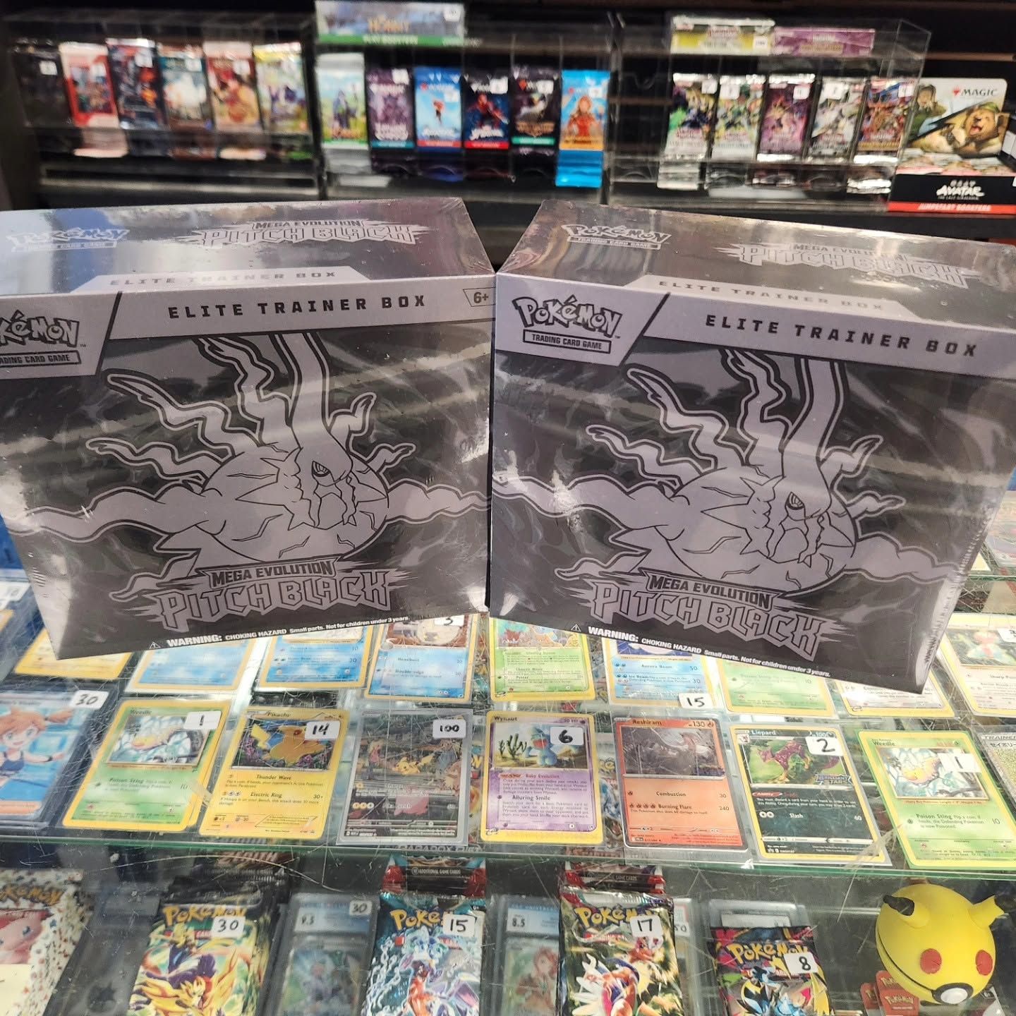 Two Pokémon Elite Trainer Boxes displayed behind a spread of colorful Pokémon cards and a Pikachu figure