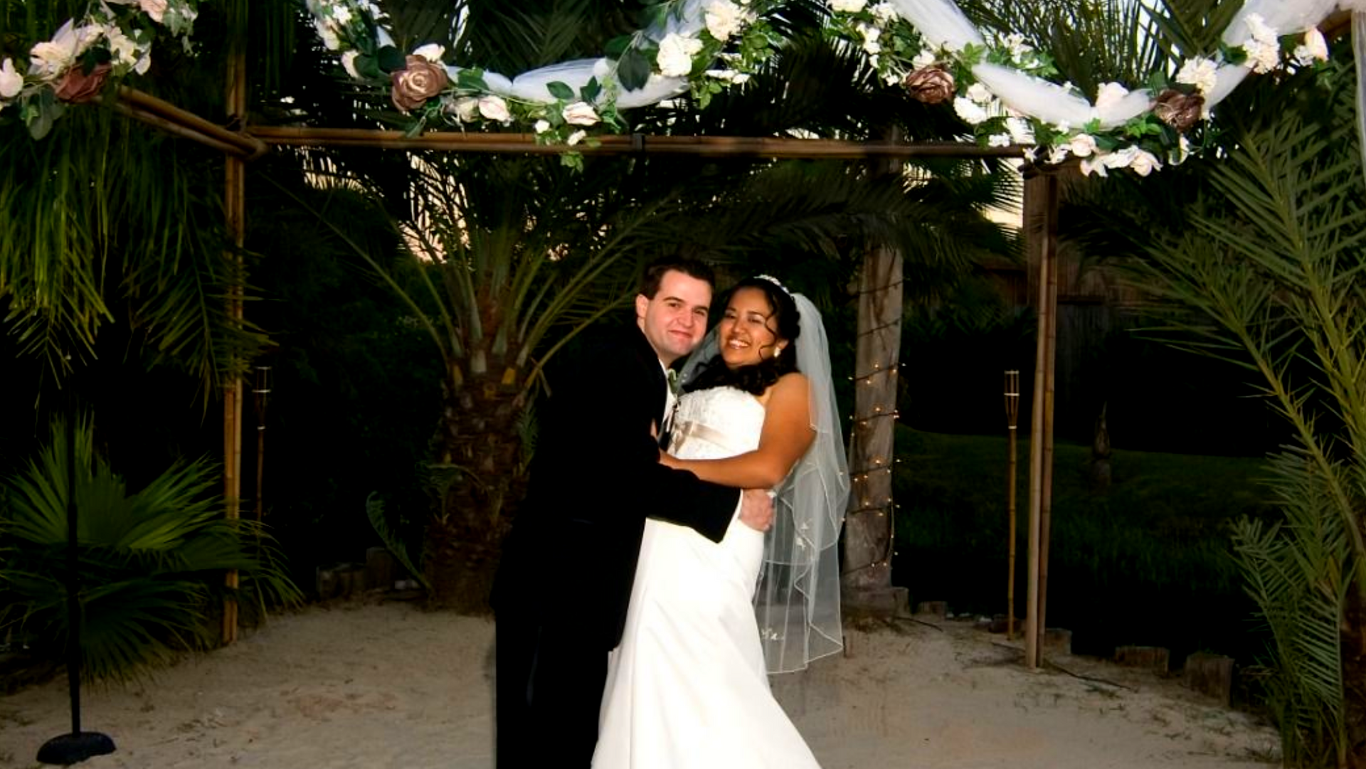Couple cutting a white wedding cake with blue flowers at a reception table