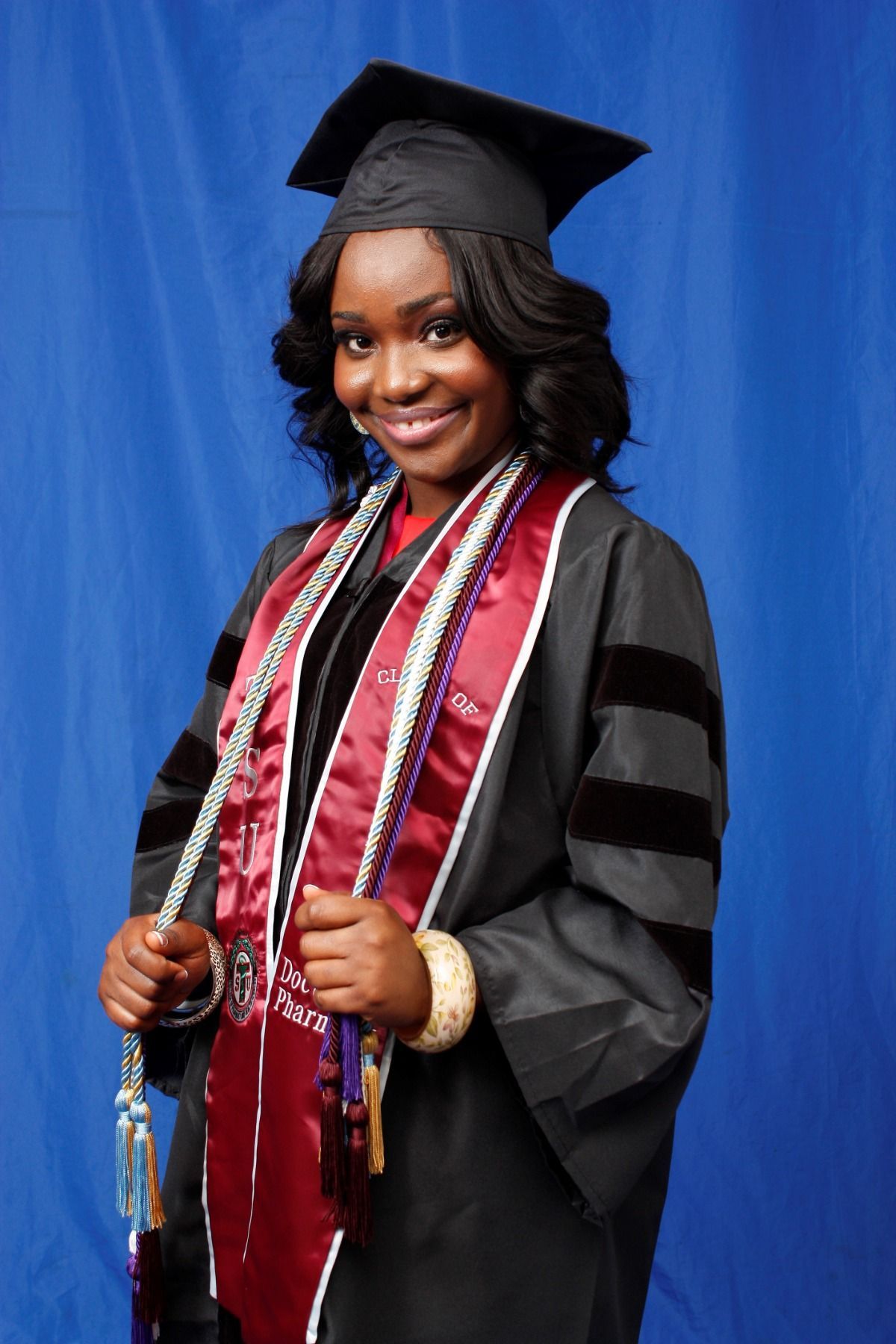 Graduate in cap and gown posing with diploma against a blue backdrop