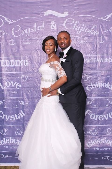 Couple in formal wedding attire posing before a purple chalkboard backdrop with decorative writing.