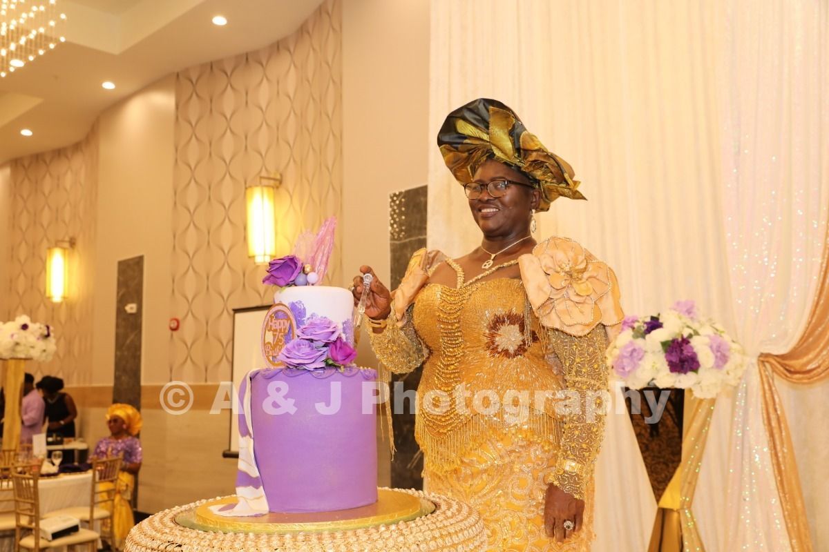 Woman in gold dress beside a purple cake at a decorated indoor celebration