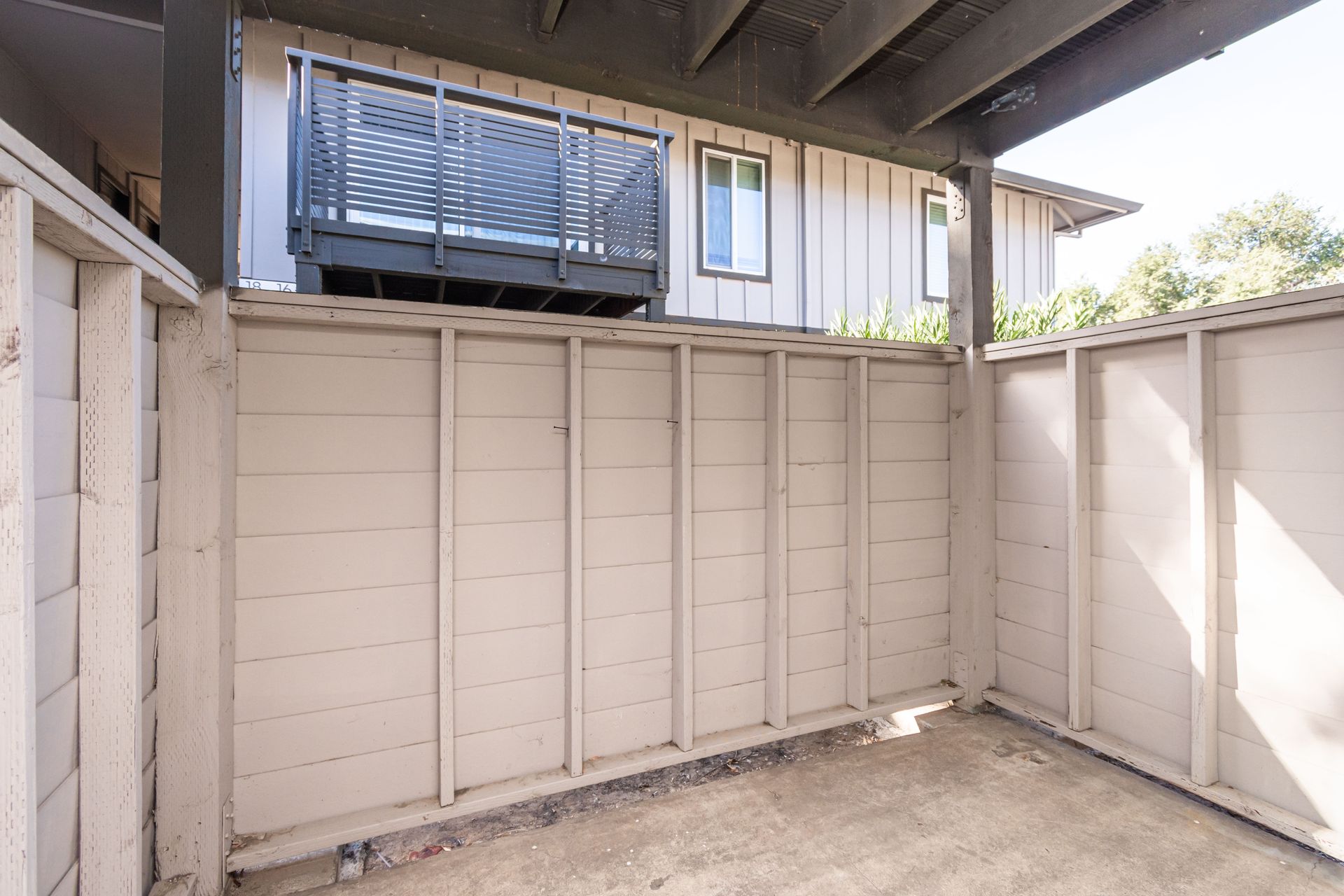 An empty patio with a fence and a balcony in front of a house.