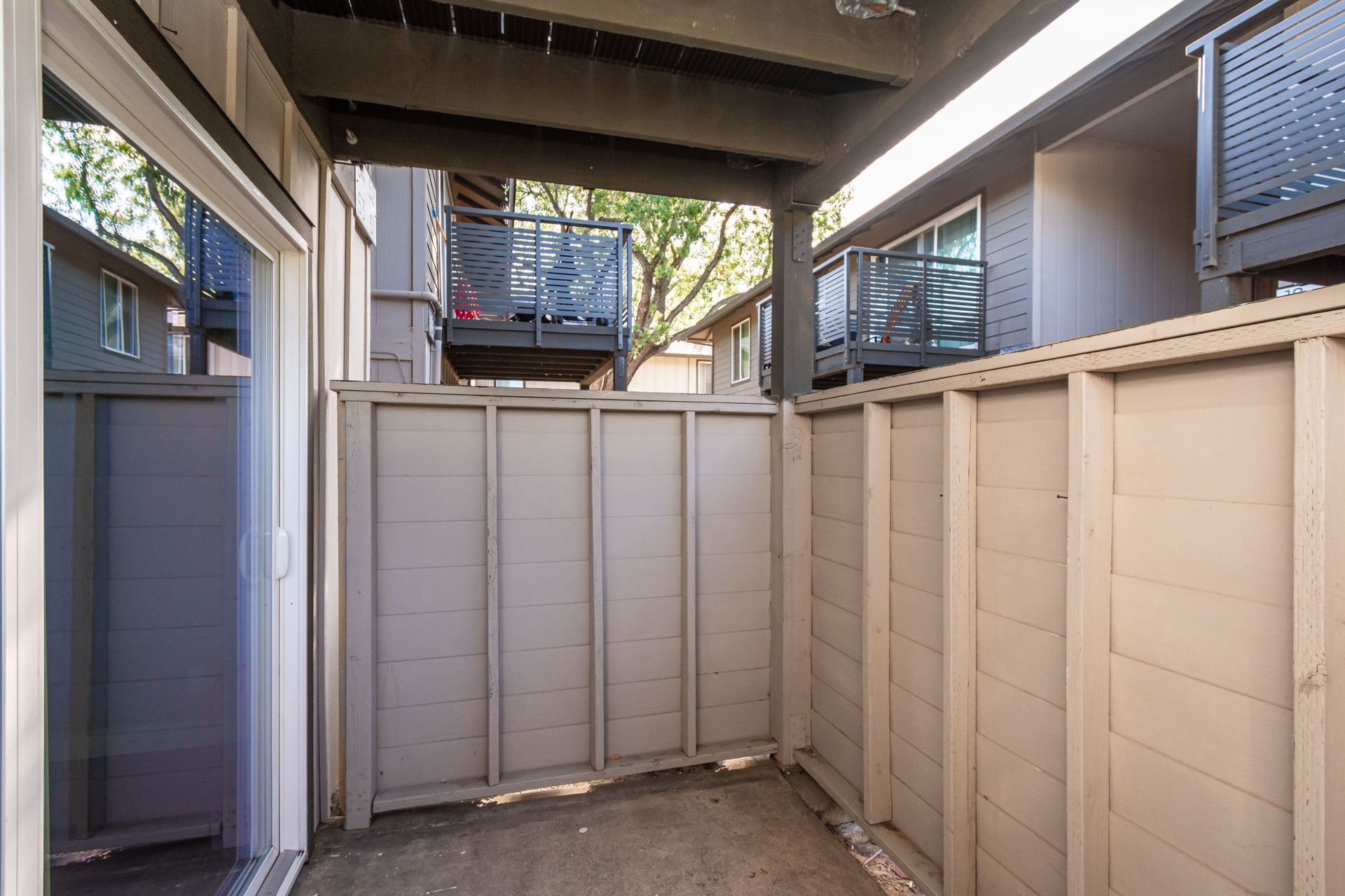 A patio with a wooden fence and sliding glass doors between two buildings.