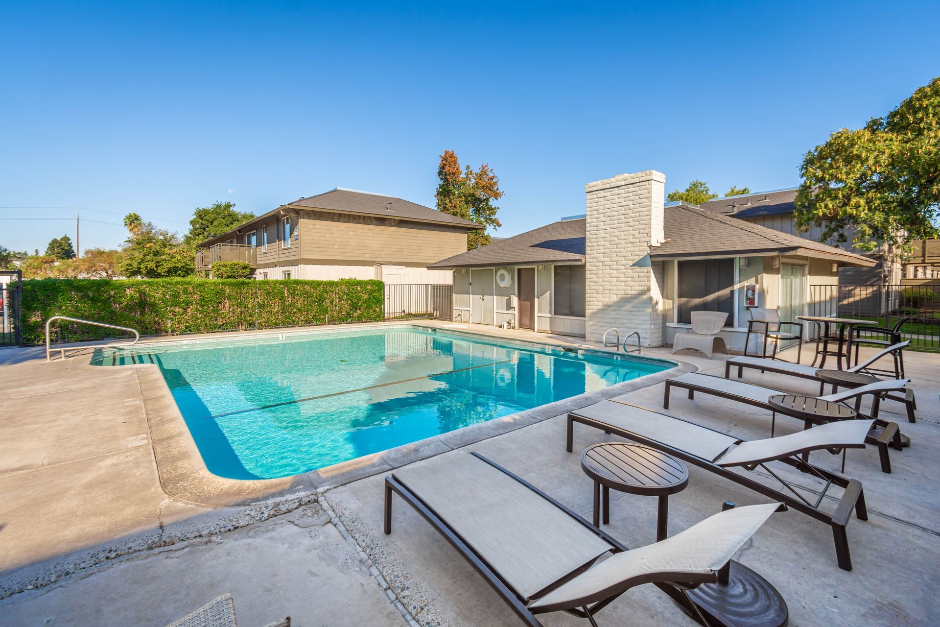 A large swimming pool surrounded by lounge chairs in front of a house.