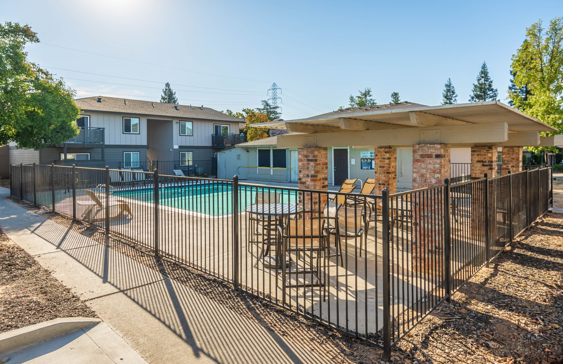 A fence surrounds a swimming pool with tables and chairs in front of a building.