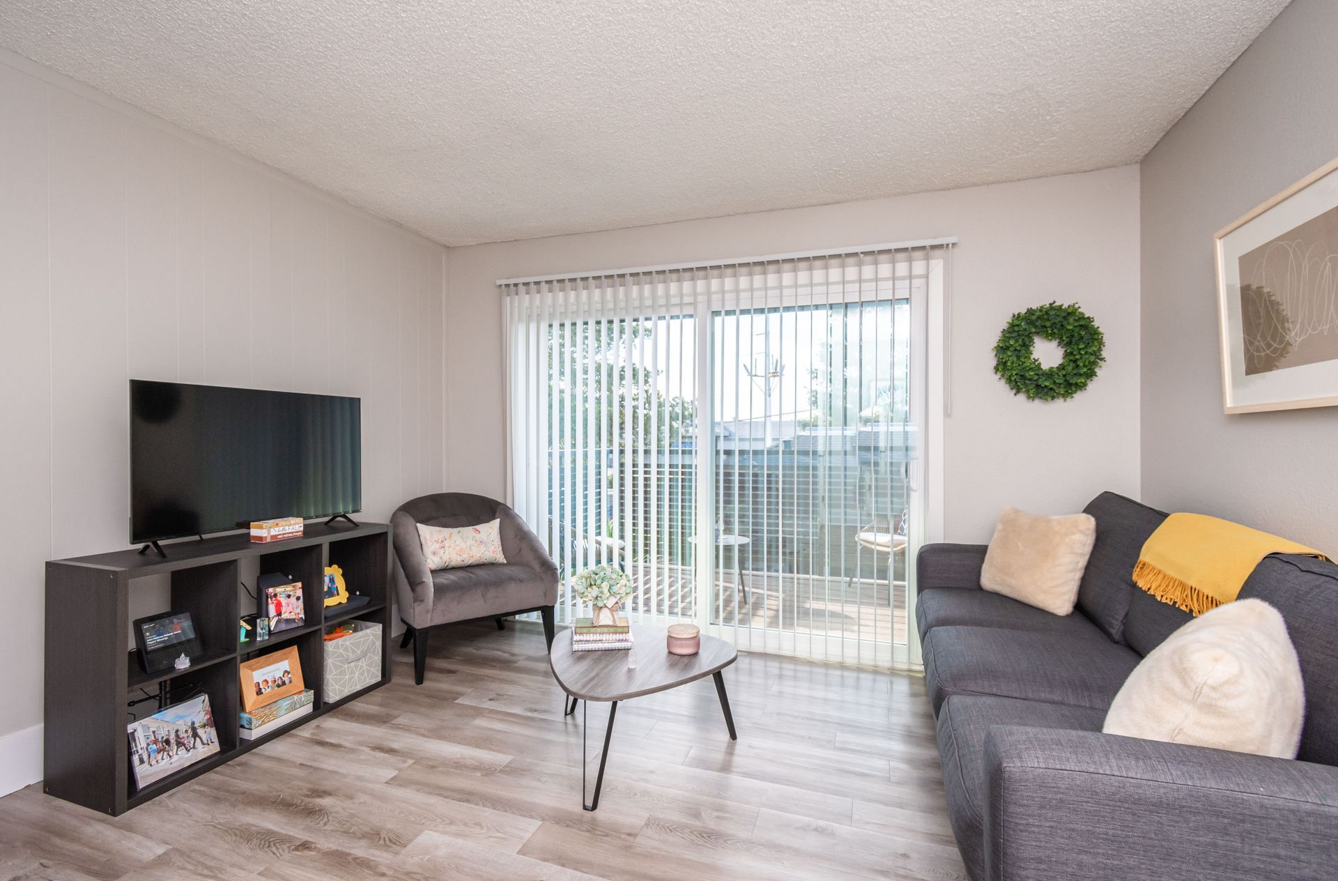 A living room with a couch , chair , television and sliding glass doors.