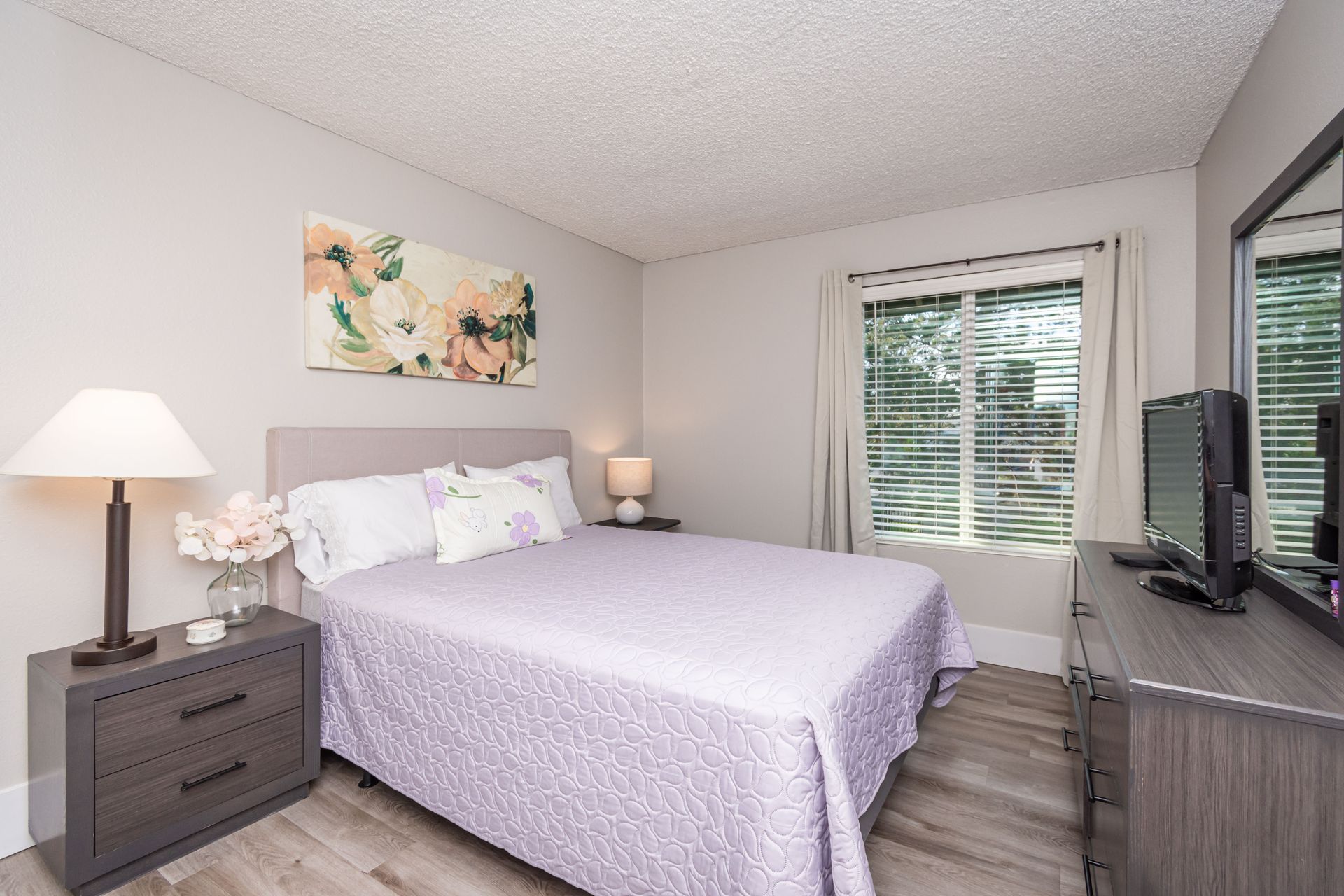 A bedroom with a king size bed , dresser , nightstand , lamp and television.