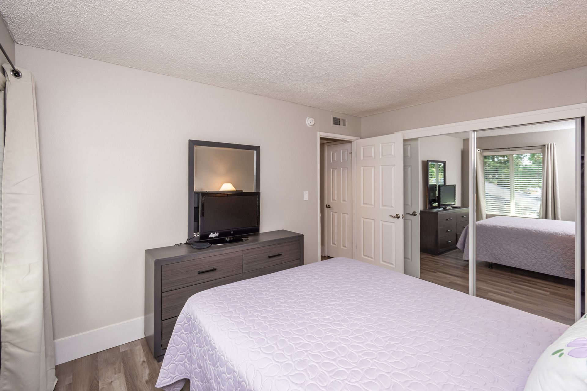 A bedroom with a king size bed , dresser , mirror and television.